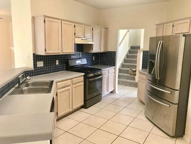 Kitchen featuring stainless steel fridge with ice dispenser, black gas range, under cabinet range hood, tasteful backsplash, and light tile patterned flooring | Image 5