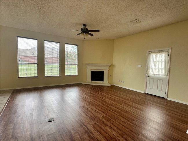Unfurnished living room featuring ceiling fan, a textured ceiling, a fireplace with raised hearth, and dark wood finished floors | Image 6