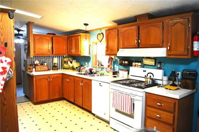 Kitchen with a textured ceiling, white appliances, exhaust hood, hanging light fixtures, and vaulted ceiling | Image 3