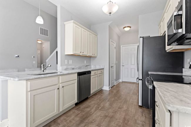 Kitchen with visible vents, appliances with stainless steel finishes, wood finished floors, a sink, and a peninsula | Image 11