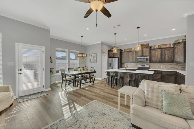 Living area with ceiling fan with notable chandelier, baseboards, visible vents, and light wood finished floors | Image 11