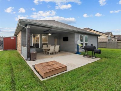 This is a well-maintained backyard with a covered patio area featuring outdoor seating and a ceiling fan, perfect for entertaining. The yard is fenced for privacy, includes a storage shed, and has ample green space for activities. A barbecue grill is also set up, enhancing the space for outdoor dining experiences. | Image 2