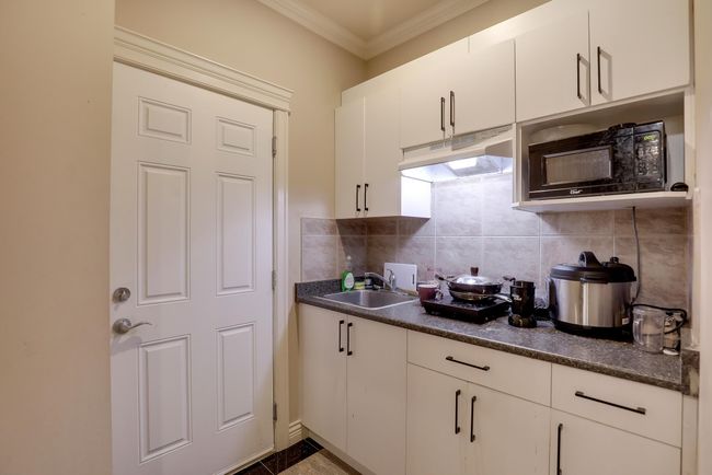 Kitchen with a sink, black microwave, dark countertops, under cabinet range hood, and ornamental molding | Image 30