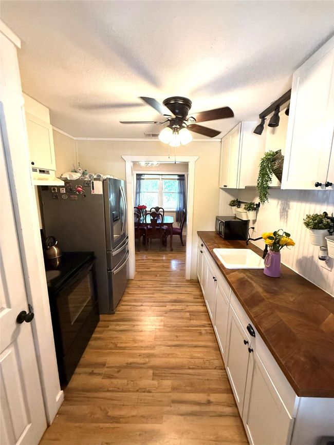 Kitchen with white cabinets, a ceiling fan, light wood-type flooring, black appliances, and under cabinet range hood | Image 16
