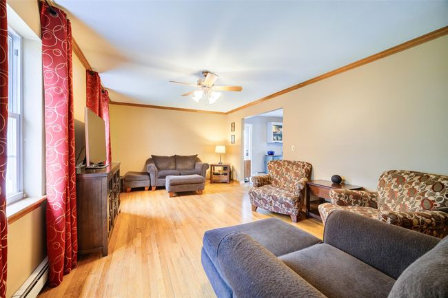 Living room featuring a baseboard heating, light wood finished floors, crown molding, and a ceiling fan | Image 5