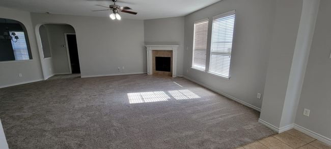 Unfurnished living room featuring ceiling fan, light carpet, arched walkways, and a tiled fireplace | Image 18