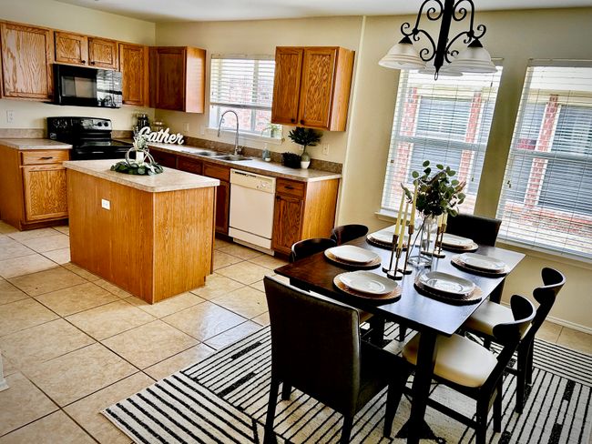 Kitchen with black appliances, a kitchen island, light countertops, brown cabinets, and light tile patterned floors | Image 13