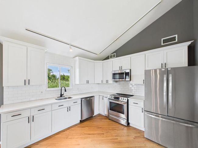 Kitchen featuring appliances with stainless steel finishes, white cabinetry, light countertops, backsplash, and lofted ceiling | Image 8