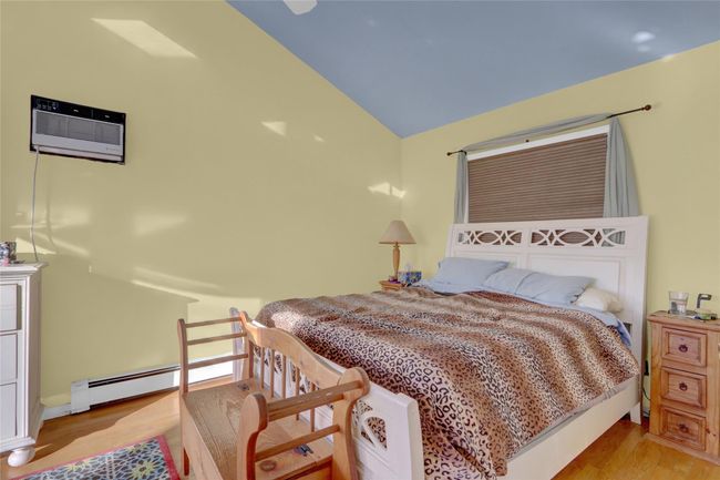 Bedroom with light wood-type flooring, lofted ceiling, a wall mounted air conditioner, and baseboard heating | Image 25