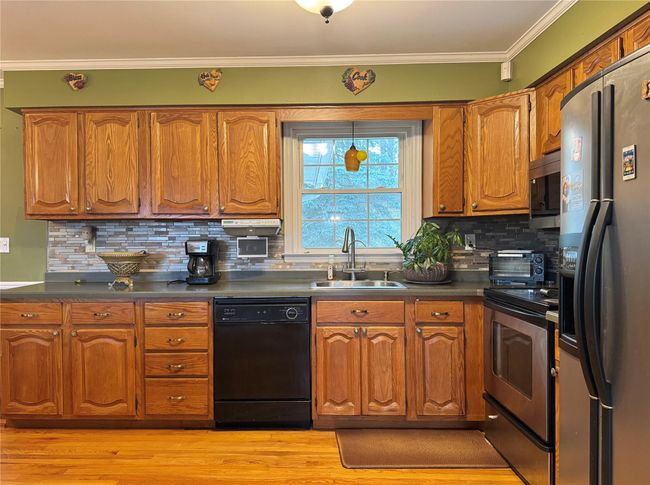 Kitchen with brown cabinets, appliances with stainless steel finishes, a sink, and dark countertops | Image 7