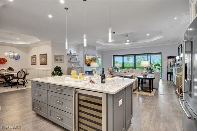 Large island featuring light wide plank tile flooring, wine cooler, tray ceiling | Image 5