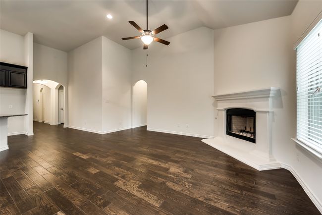 Unfurnished living room with arched walkways, ceiling fan, dark wood-style floors, a fireplace with raised hearth, and high vaulted ceiling | Image 10