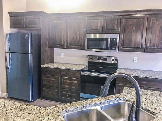 Kitchen with light stone counters, stainless steel appliances, dark brown cabinets, wood finished floors, and a sink | Image 24