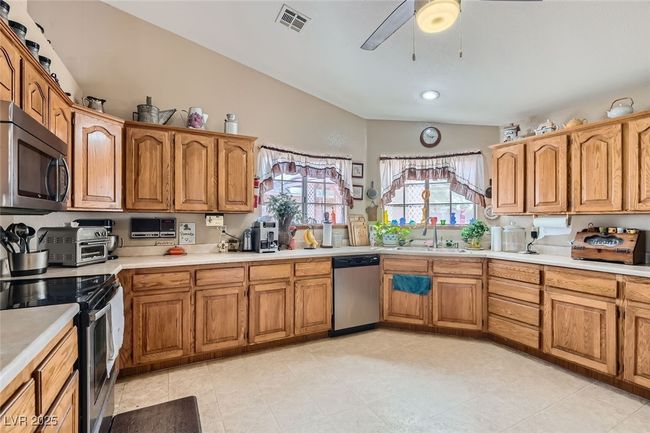 Kitchen with stainless steel appliances, lofted ceiling, light countertops, visible vents, and a sink | Image 12