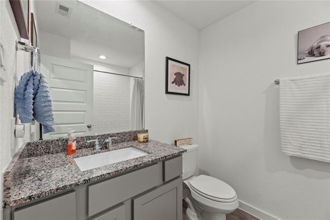 The bathroom features a sleek, modern design with a single vanity topped with beautiful granite countertops. A square, contemporary sink sits above the countertop, paired with a stylish nickel faucet that adds a touch of elegance. The light-colored walls create a fresh, airy feel, complementing the clean lines of the space. Above the sink, a large frameless mirror enhances the openness of the room, reflecting light and creating a bright, spacious atmosphere. This bathroom is both functional and chic. | Image 16