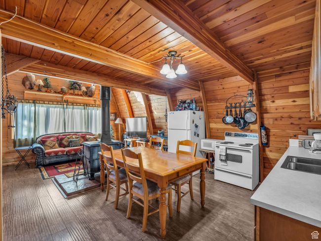 Dining room with a wood stove, wooden walls, a wood ceiling with exposed beams, a chandelier, and dark wood-style floors | Image 9