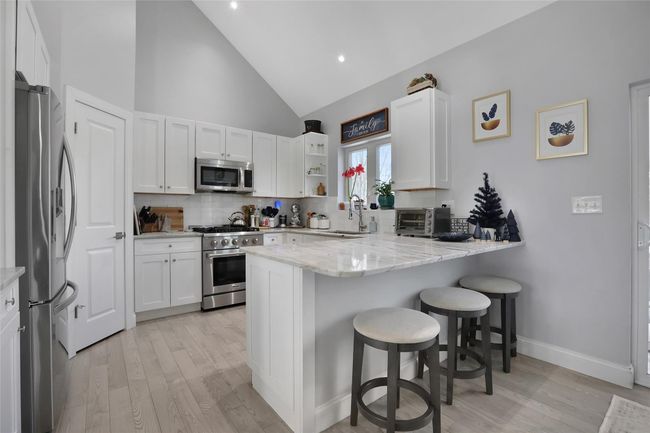 Kitchen featuring white cabinets, a kitchen breakfast bar, appliances with stainless steel finishes, tasteful backsplash, and kitchen peninsula | Image 6