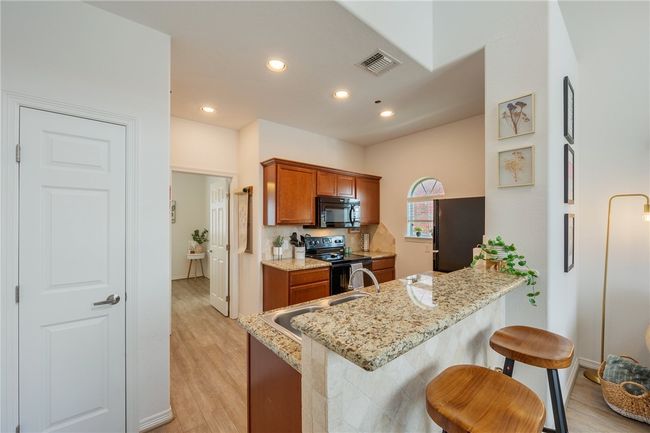 Kitchen featuring black appliances, brown cabinets, a peninsula, light stone counters, and a breakfast bar area | Image 7