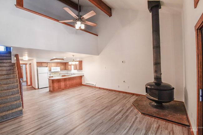 Unfurnished living room featuring light wood-style floors, a baseboard heating unit, stairway, beamed ceiling, and a ceiling fan | Image 6