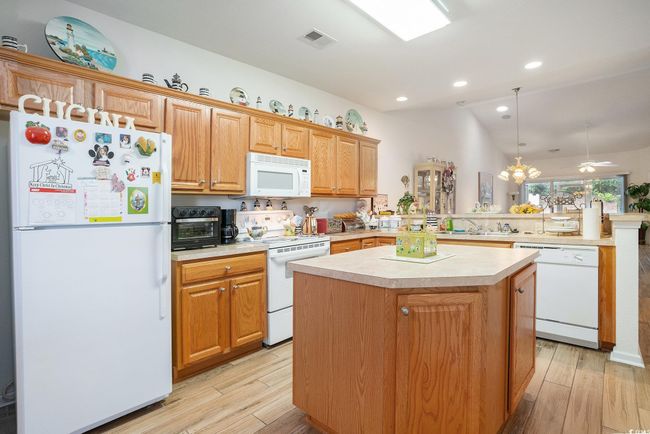 Kitchen with white appliances, a peninsula, light countertops, a kitchen island, and light wood-style floors | Image 5