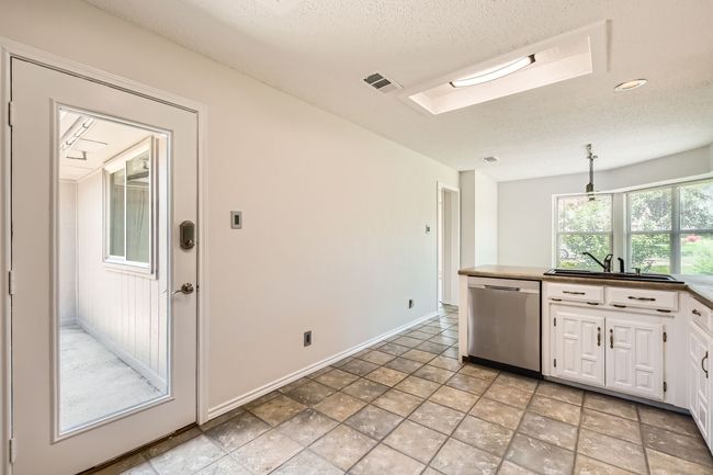 Kitchen with stainless steel dishwasher, white cabinets, a skylight, and a textured ceiling | Image 8