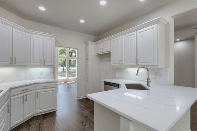 Kitchen featuring a sink, dark wood-style flooring, a peninsula, white cabinetry, and light stone counters | Image 13