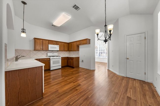 Kitchen with a sink, visible vents, white appliances, and brown cabinetry | Image 7