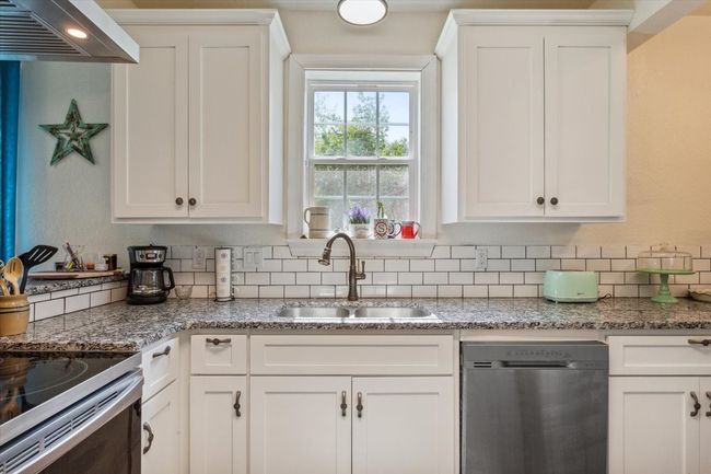 Kitchen featuring a sink, wall chimney range hood, stainless steel dishwasher, and white cabinets | Image 11