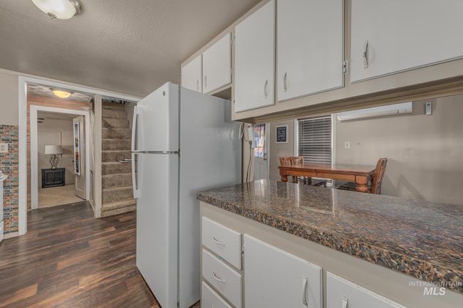 Kitchen with freestanding refrigerator, dark wood-style floors, white cabinets, dark countertops, and a textured ceiling | Image 11