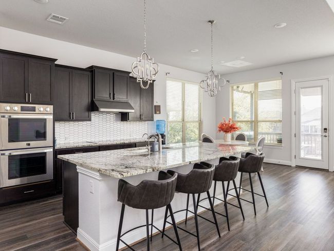 Kitchen with visible vents, a chandelier, under cabinet range hood, double oven, and a breakfast bar area | Image 8
