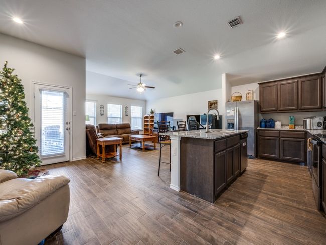 Kitchen featuring open floor plan, dark brown cabinetry, a breakfast bar, light stone countertops, and recessed lighting | Image 5