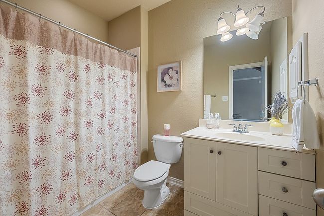 Full bathroom featuring tile patterned floors, a shower with shower curtain, toilet, a textured wall, and vanity | Image 29