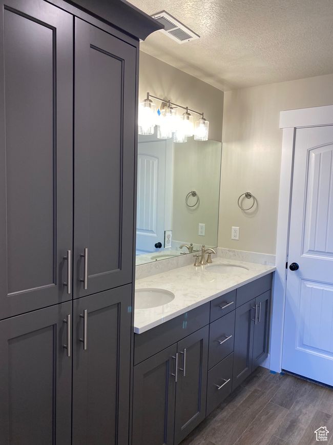 Full bath with wood finished floors, a sink, a textured ceiling, double vanity, and visible vents | Image 15
