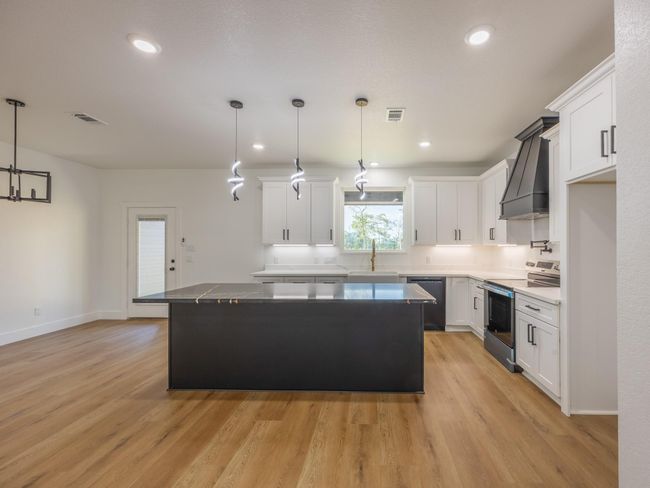Crisp white cabinetry, quartz countertops, and black hardware create a clean and timeless look. The spacious island adds prep space and seating while stylish pendant lights offer a contemporary touch. | Image 13
