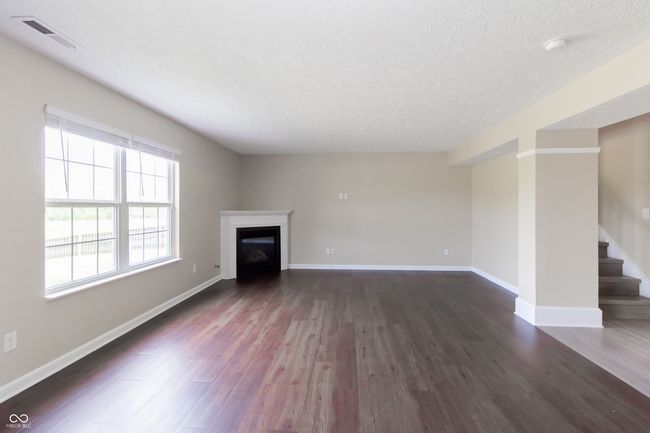 unfurnished living room with dark wood-style flooring, a textured ceiling, stairway, and a glass covered fireplace | Image 4