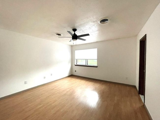 Empty room with light wood finished floors, a ceiling fan, and a textured ceiling | Image 10