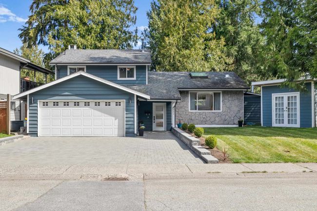 Tri-level home with decorative driveway, a front yard, stone siding, an attached garage, and french doors | Image 4