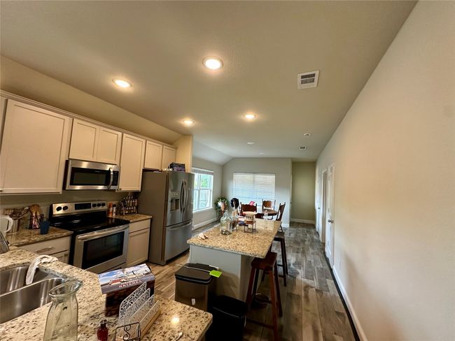 Kitchen featuring stainless steel appliances, wood finished floors, a kitchen bar, lofted ceiling, and a kitchen island | Image 12