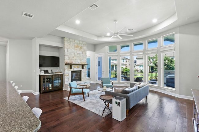 Living room featuring a raised ceiling, floors, a stone fireplace, a ceiling fan, and recessed lighting | Image 12