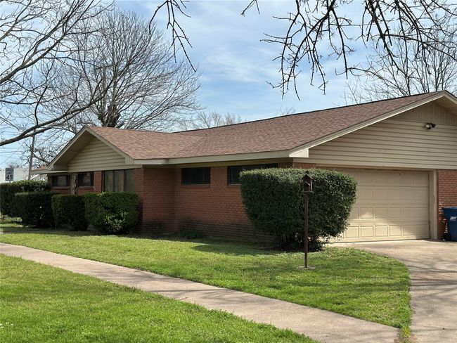 View of property exterior with driveway, a yard, roof with shingles, an attached garage, and brick siding | Image 16