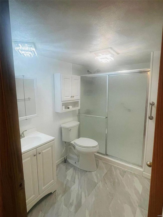 Full bath featuring vanity, toilet, a textured ceiling, a shower stall, and marble finish floor | Image 7