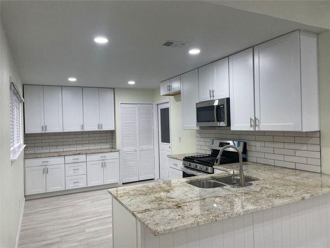 Kitchen with appliances with stainless steel finishes, light stone countertops, light wood-type flooring, a sink, and white cabinetry | Image 20