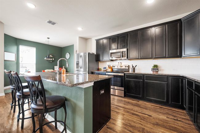 Kitchen featuring stainless steel appliances, dark stone countertops, dark wood-style flooring, a center island with sink, and recessed lighting | Image 7