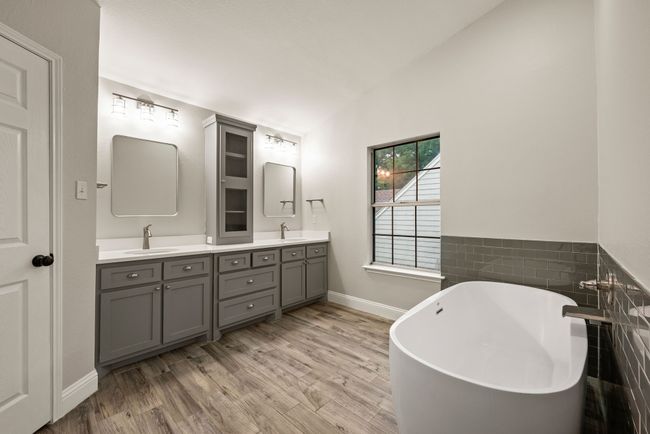 This primary bathroom is truly a standout! Dual vanities with upgraded cabinetry and lighting, a luxurious freestanding soaking tub, and a glass-enclosed tiled shower — all in soothing gray and white tones. | Image 24