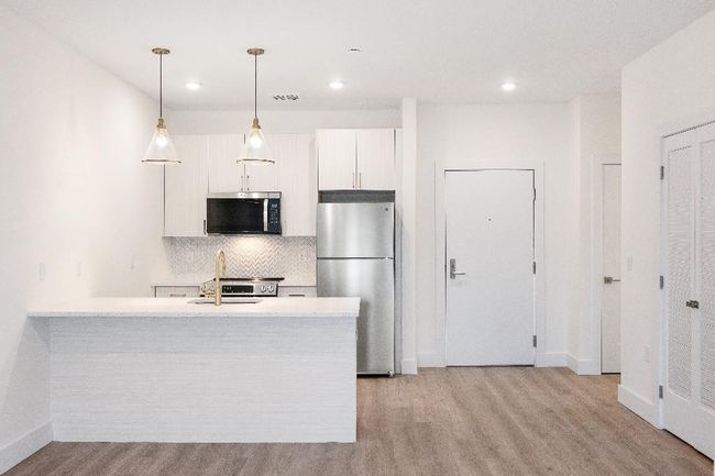 Kitchen featuring appliances with stainless steel finishes, backsplash, light countertops, light wood finished floors, and white cabinets | Image 33