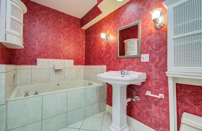 Luxurious primary bath featuring a deep soaking tub, elegant pedestal sink, and vibrant decor for a spa-like retreat. | Image 18