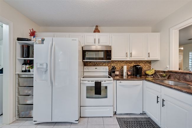 Kitchen featuring white appliances, white cabinets, light tile patterned floors, backsplash, and dark stone countertops | Image 9