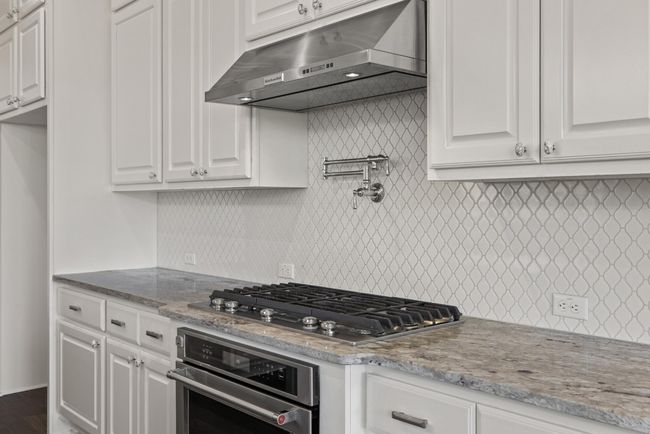 Kitchen featuring under cabinet range hood, stainless steel appliances, white cabinetry, and decorative backsplash | Image 8