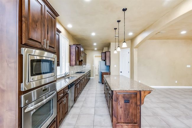 Kitchen with decorative backsplash, light stone countertops, stainless steel appliances, a kitchen island, and a sink | Image 14