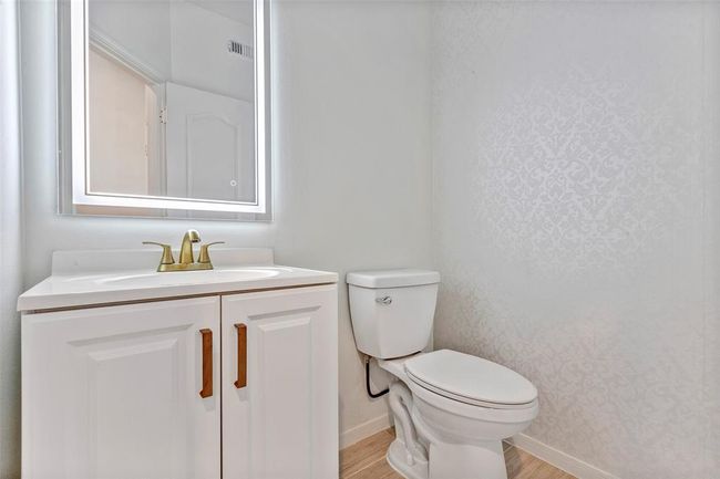 This bathroom features a modern design with a white vanity, a sleek mirror, and a toilet. The subtle patterned wallpaper adds a touch of elegance. | Image 12